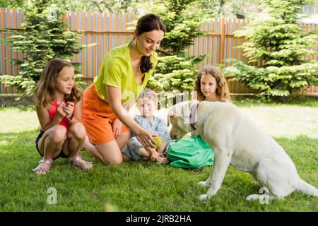 Smiling mother showing ball to dog by daughters at back yard Stock Photo
