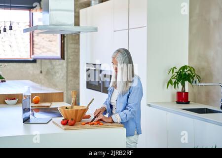 Mature woman cutting carrots on kitchen counter Stock Photo