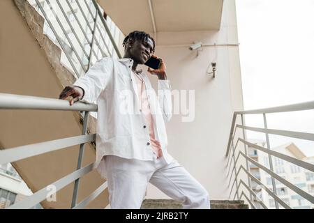 Smiling young man talking on phone standing by railing Stock Photo