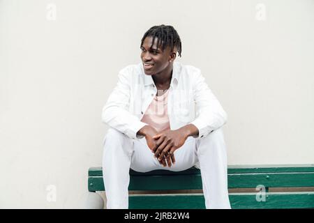 Smiling young man with dreadlocks sitting on bench Stock Photo