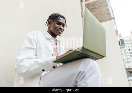 Smiling man using laptop by wall Stock Photo