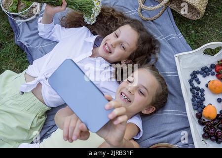 Happy sisters taking selfie on smart phone lying in park Stock Photo