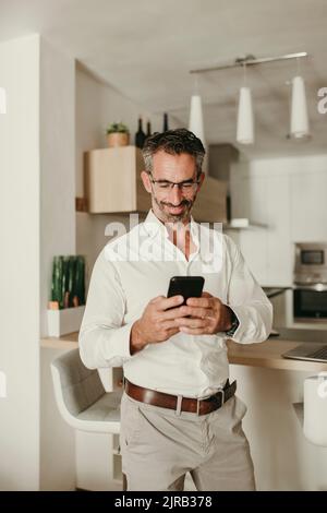Smiling businessman using mobile phone at home Stock Photo