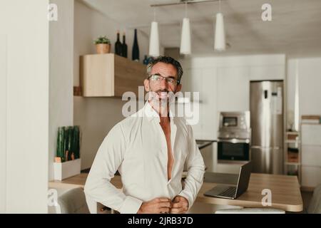 Businessman buttoning shirt in kitchen at home Stock Photo