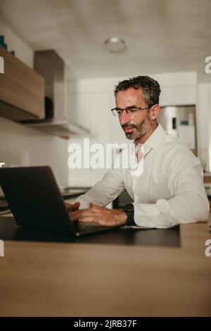 Mature businessman using laptop on kitchen counter at home Stock Photo