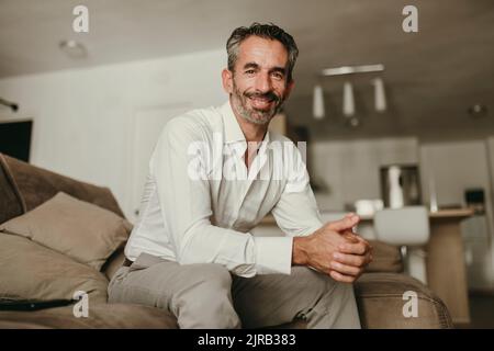 Smiling businessman sitting with hands clasped on sofa at home Stock Photo