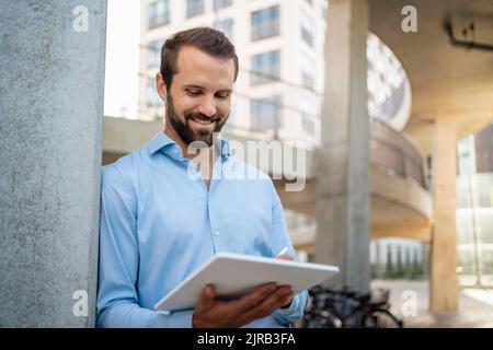 Smiling young businessman using tablet PC standing under bridge Stock Photo