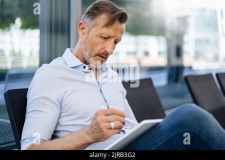 Mature businessman using graphic tablet sitting on seat Stock Photo