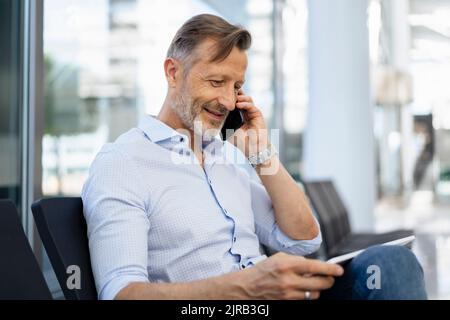 Smiling businessman talking on smart phone using graphic tablet Stock Photo