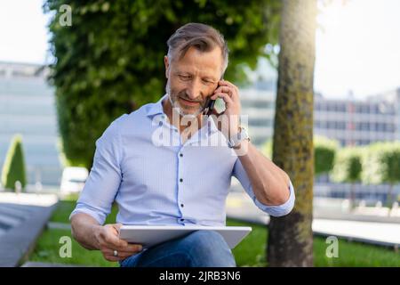 Businessman talking on smart phone using digital tablet at office park Stock Photo