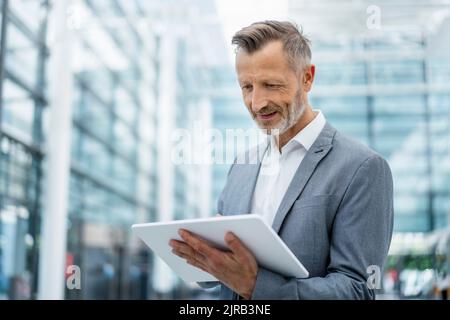 Smiling businessman in gray blazer using digital tablet Stock Photo