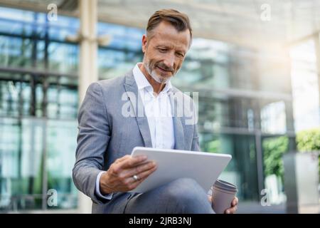 Smiling businessman holding reusable coffee cup using digital tablet Stock Photo