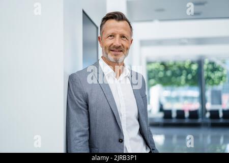 Smiling mature businessman leaning on white wall Stock Photo