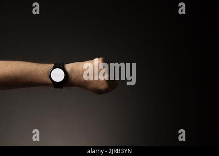 Man's hand with smart watch on wrist, displaying blank white screen, isolated on dark background with copy space Stock Photo