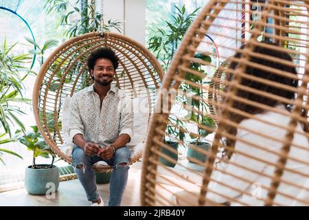 Businessman and businesswoman sitting in hanging chairs talking to each other Stock Photo