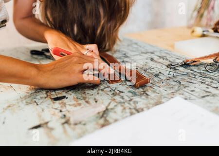 Hands of craftsperson making leather accessory at workshop Stock Photo