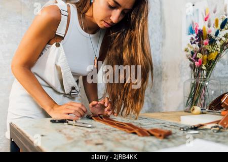 Young craftsperson making leather accessory at workshop Stock Photo