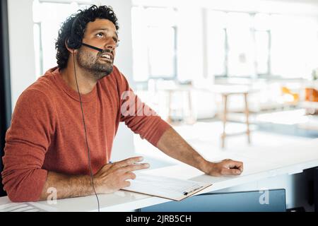 Thoughtful businessman with headset sitting at workplace Stock Photo