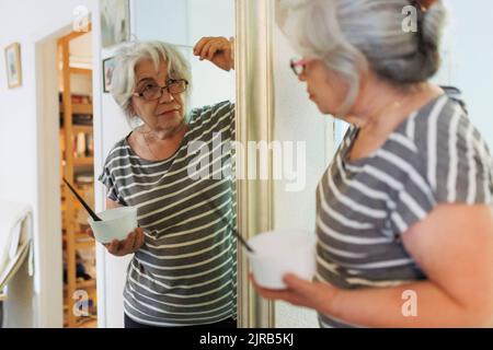 Senior woman examining white hair looking in mirror at home Stock Photo