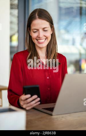 Smiling businesswoman using smart phone at work place Stock Photo
