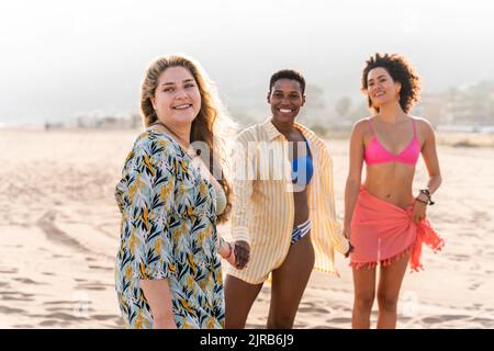 Smiling multiracial friends holding hands standing at beach Stock Photo