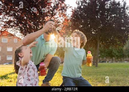 Man blowing bubbles by son and daughter at park Stock Photo