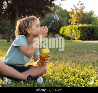 Boy blowing bubbles sitting at park Stock Photo