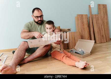 Man with son reading instruction manual sitting on floor at home Stock Photo