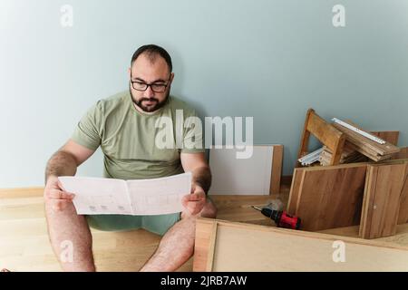 Man reading instruction manual sitting on floor at home Stock Photo