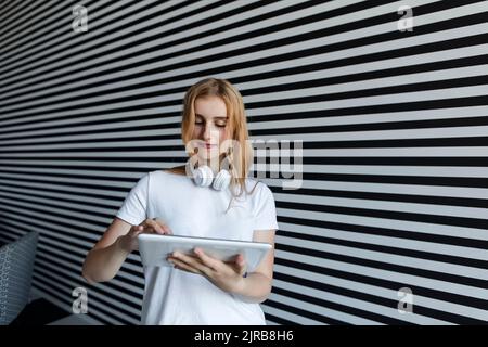 Girl with headphones using tablet PC in front of striped wall Stock Photo