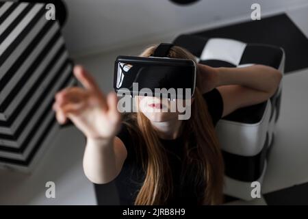 Teenage girl wearing virtual reality headset gesturing with hand raised Stock Photo