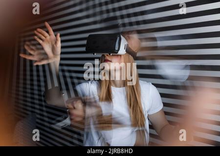 Teenage girl wearing virtual reality headset gesturing by striped wall Stock Photo