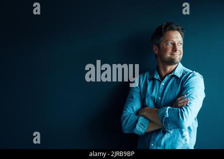 Smiling businessman standing with arms crossed against blue background Stock Photo