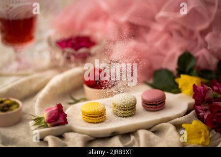 A closeup shot of colorful macarons on the metallic plate with flowers and other decorations around Stock Photo