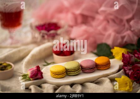 A closeup shot of colorful macarons on the metallic plate with flowers and other decorations around Stock Photo