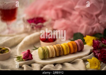 A closeup shot of colorful macarons on the metallic plate with flowers and other decorations around Stock Photo