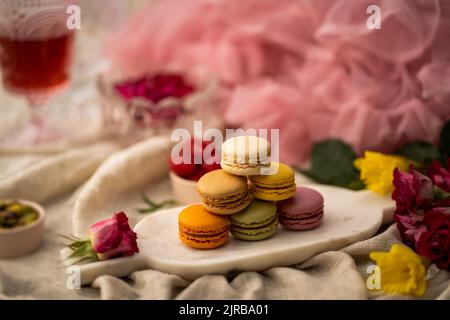 A closeup shot of colorful macarons on the metallic plate with flowers and other decorations around Stock Photo