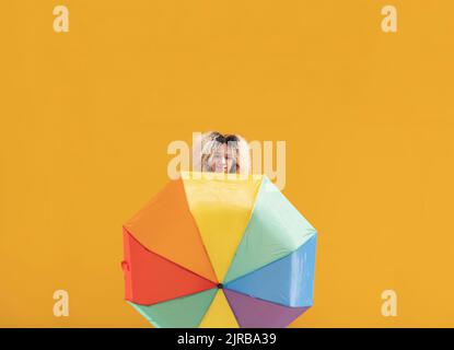 Smiling young woman with multi colored umbrella in front of yellow wall on sunny day Stock Photo