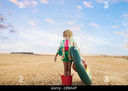 Young woman standing with avocado shaped inflatable ring at field Stock Photo