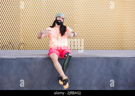 Bearded man with prosthetic leg sitting on wall Stock Photo
