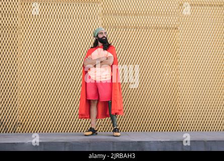 Bearded man with prosthetic leg wearing cape standing in front of wall Stock Photo