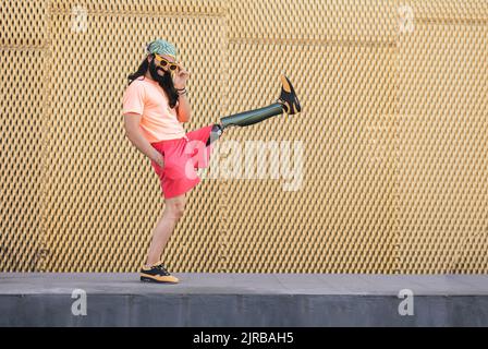 Smiling hipster man with prosthetic leg kicking in front of wall Stock Photo