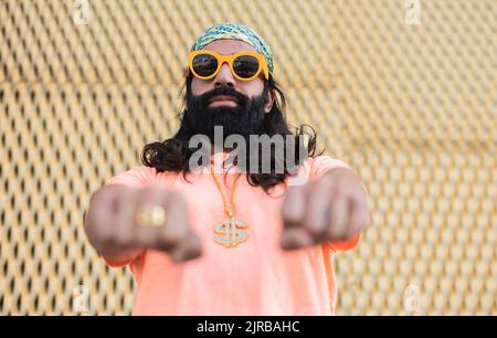 Bearded man wearing sunglasses gesturing fists in front of wall Stock Photo