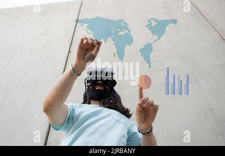 Smiling bearded man wearing VR glasses touching maps and chart Stock Photo