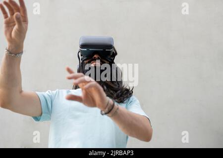 Smiling bearded man wearing virtual reality simulator in front of wall Stock Photo