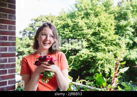 Happy girl holding fresh radishes on balcony Stock Photo