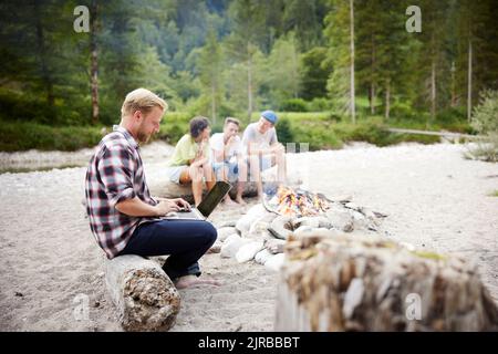 Businessman using laptop sitting on log with friends in background Stock Photo