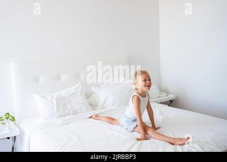 Happy girl doing splits on bed at home Stock Photo