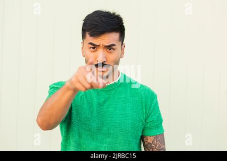 Young man with serious expression pointing in front of wall Stock Photo
