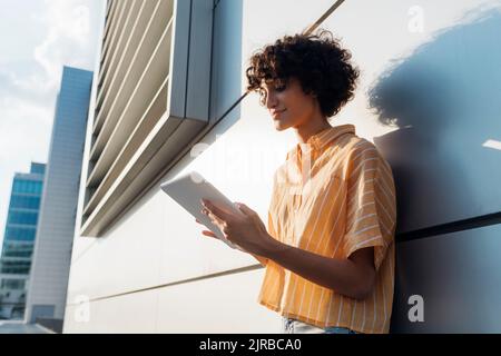 Smiling young freelancer using tablet PC by wall Stock Photo